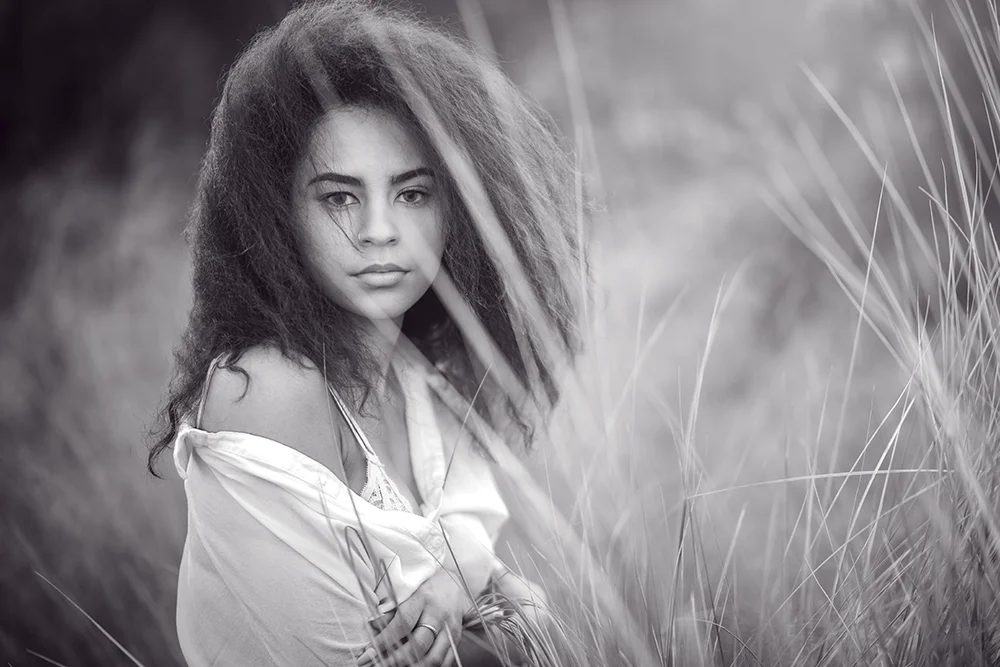 Outdoor black and white informal portrait of young woman in a tall grass field