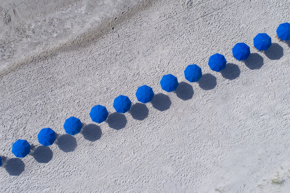 A diagonal line of blue beach umbrellas as viewed from directly overhead