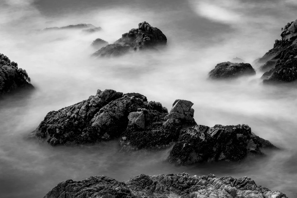Cliffside boulders with blurred wave in Pacific Ocean