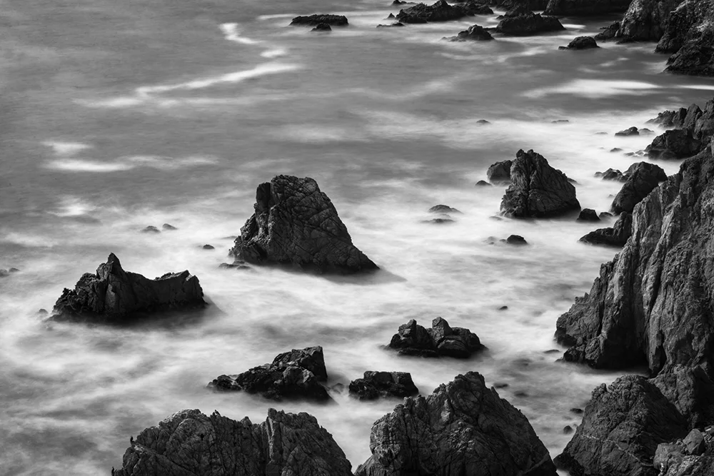 Long Exposure image of Pacific coastline with multiple boulders and blurred waves.