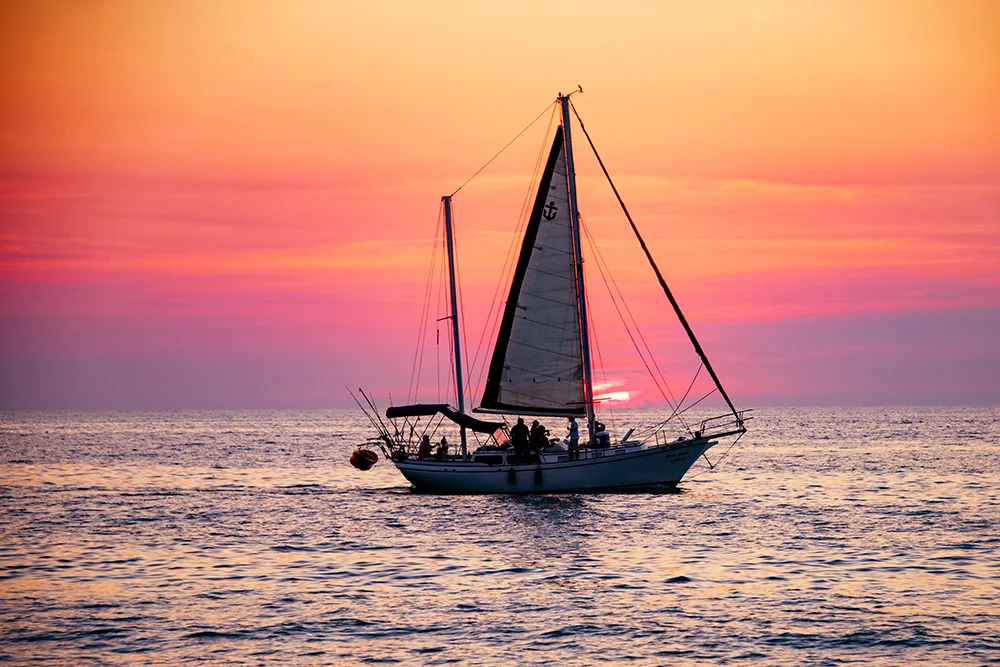 A pink and yellow sunset behind a silhouetted sailboat on the Pacific Ocean
